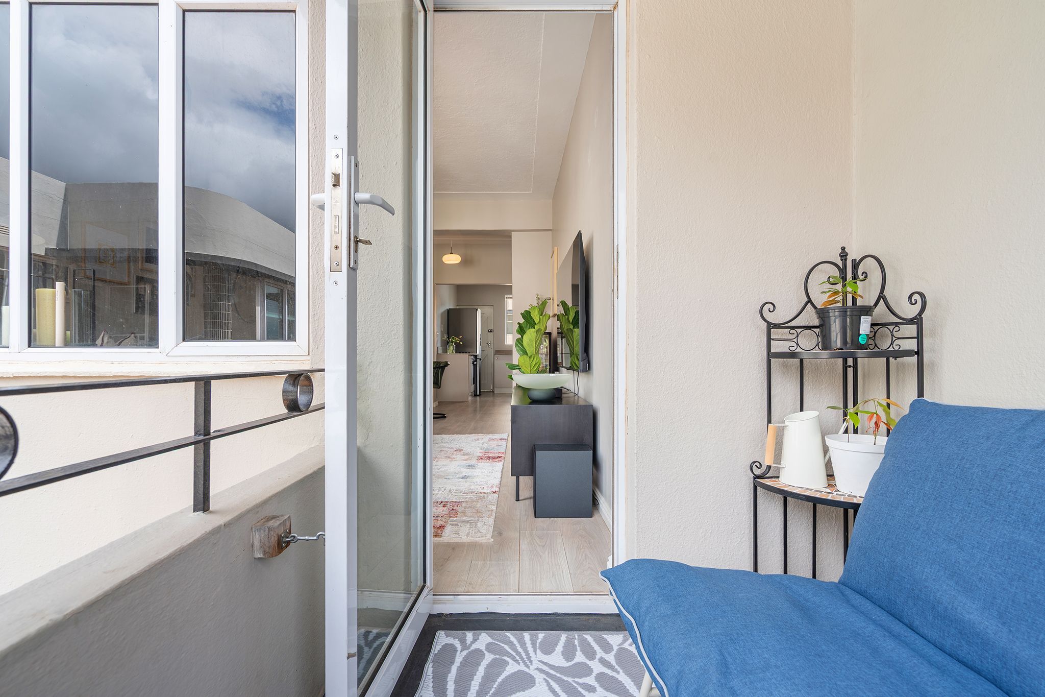 A balcony with a blue sofa, a potted plant, and a small table with a white container.