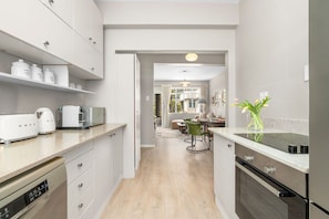 A modern kitchen with white cabinetry, a dishwasher, a stove, and a dining area with a table and chairs. - Fairmont 22 on Hof (Cape Town)