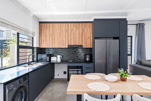 A modern kitchen with a dishwasher, oven, and a dining area with a table and chairs. - Woodlands Estate 22 (Ballito)