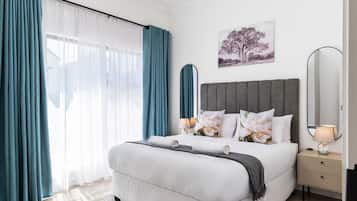 A bedroom with a bed, a bedside table, a lamp, a mirror, and a window with curtains.