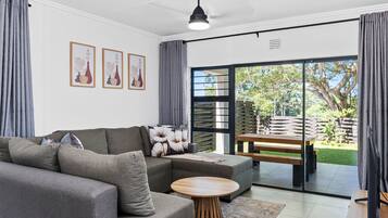 A modern living room with a sectional sofa, a round wooden coffee table, and a sliding glass door leading to a garden.
