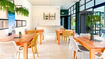 A modern interior with wooden tables and chairs, a reception desk, and green plants.