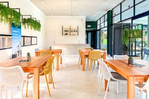 A modern interior with wooden tables and chairs, a reception desk, and green plants.