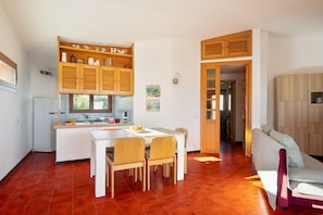 A modern kitchen with wooden cabinets, a dining area with a white table and chairs, and a cozy seating area with a sofa. - Arvella Stay II by Klodge, Bados beachfront terrace (Olbia)
