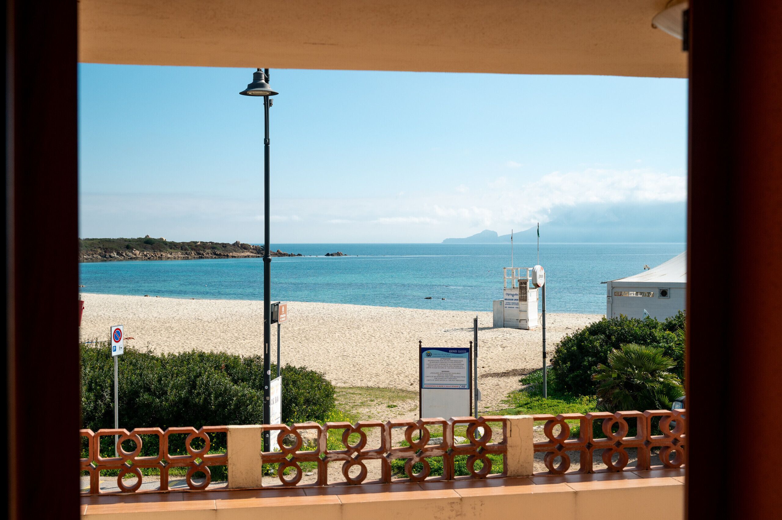 A beach view from a balcony with a railing, a lamp post, and a signboard.