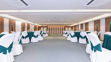A conference room with rows of white chairs with teal sashes, tables with green tablecloths, and a wooden panel wall with vertical stripes.