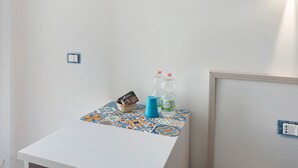 Uma pequena mesa com toalha de mesa colorida, um cesto, uma xícara azul e duas garrafas de água.
