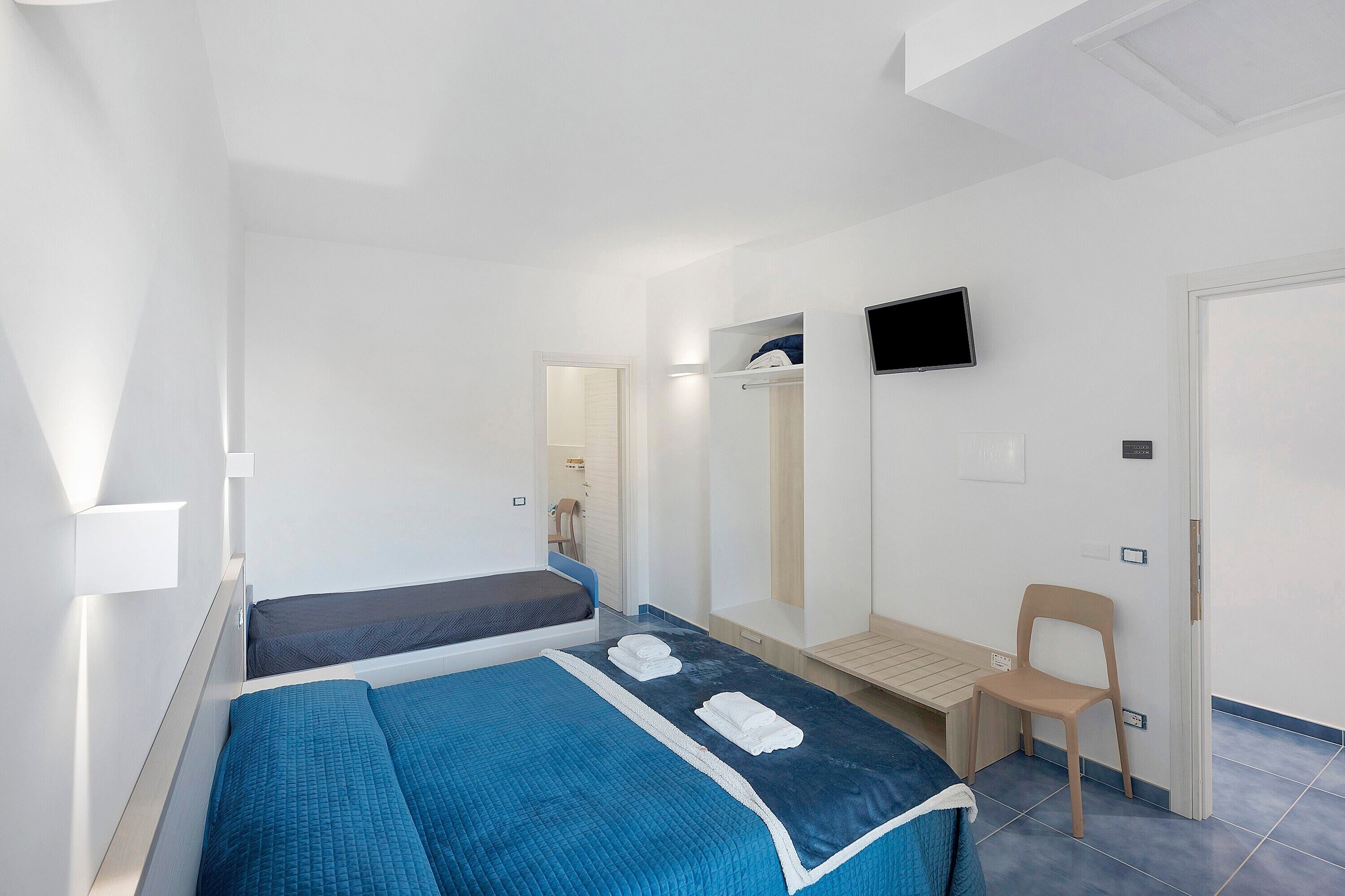 A bedroom with two beds, a TV, a mirror, and a chair.