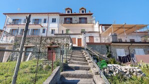 Um edifício de vários andares com escadas que levam a uma porta, cercado por vegetação e uma cerca.