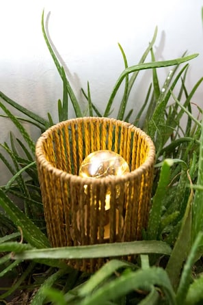 A wicker candle holder with a clear glass bulb in the center, surrounded by green grass. - Athens Central Jacuzzi Retreat (Athens)
