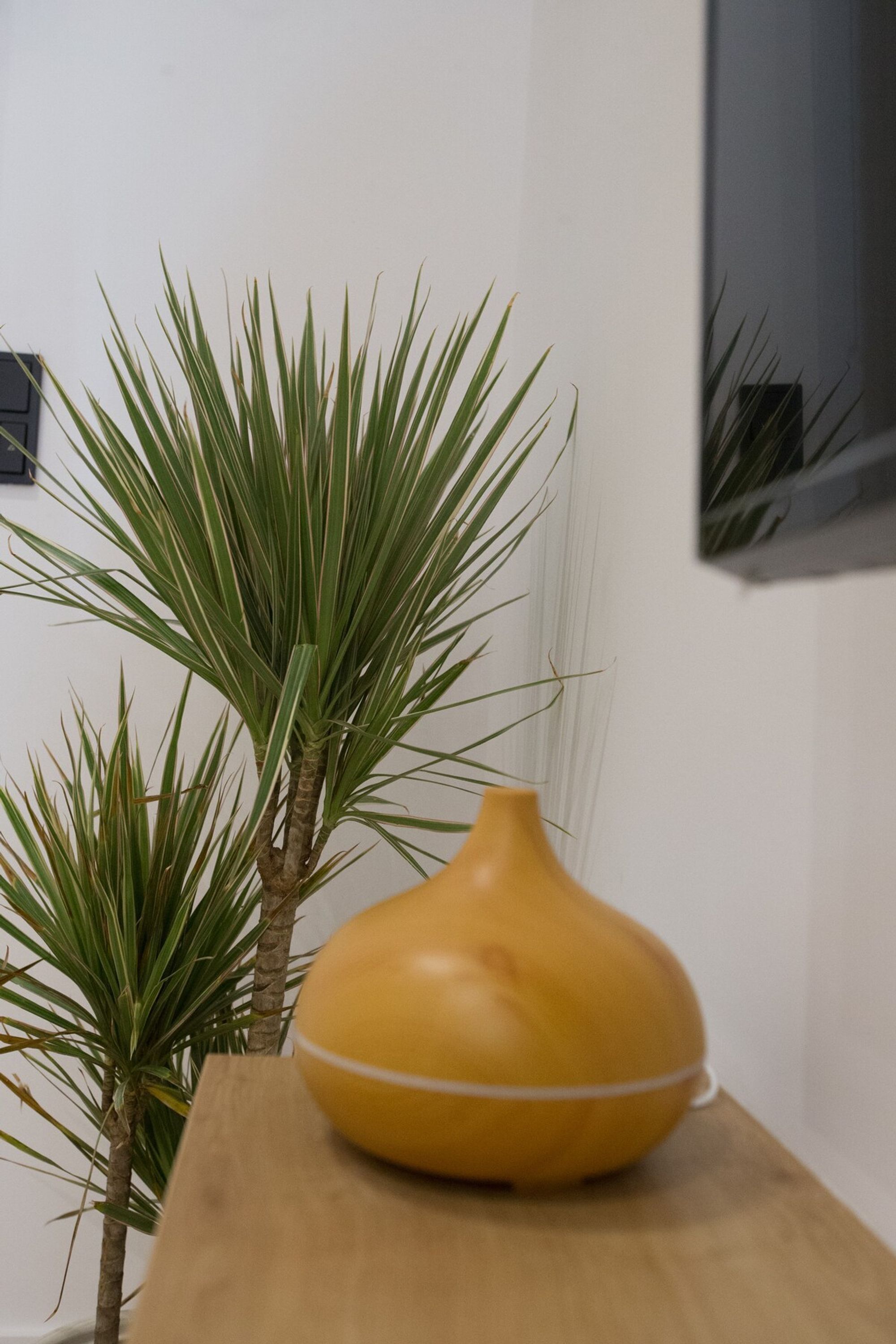 A yellow vase on a wooden table with a potted plant beside it.