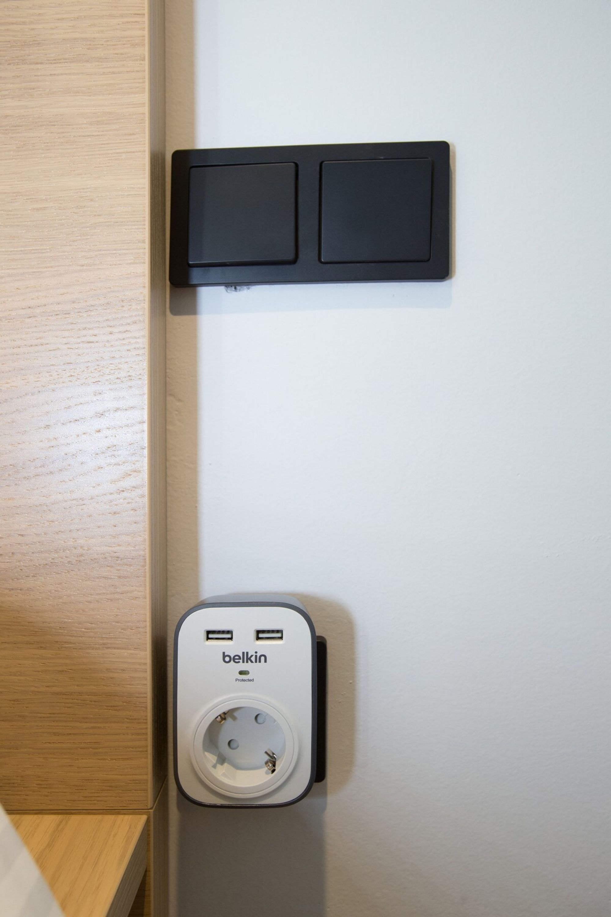 A wall-mounted power outlet with a Belkin brand charger, two USB ports, and a wall socket.