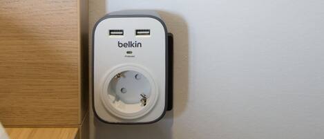 A wall-mounted power outlet with a Belkin brand charger, two USB ports, and a wall socket.