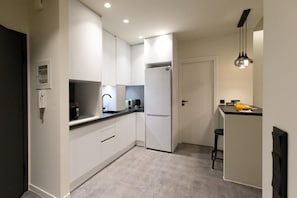 A compact kitchen with white cabinets, a refrigerator, a coffee machine, and a bar area with stools. - Acropolis Modern House (Athens)
