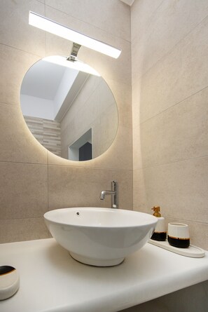 Ein modernes Badezimmer mit einem runden weißen Waschbecken, einem rechteckigen Spiegel und einer Leuchte darüber.