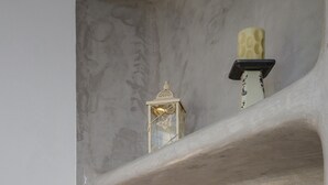 Ein Badezimmer mit Marmorwand, einer kleinen Ablage mit Dekorationen, einer Wandleuchte und einem Glas mit blauer Flüssigkeit.