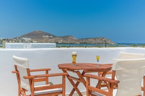 Une table et des chaises en bois sur une terrasse offrant une vue sur la montagne et la mer.