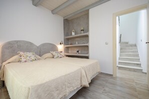 Une chambre dotée d’un grand lit, d’une étagère intégrée où sont exposés des objets décoratifs, et d’un escalier menant à un autre étage.