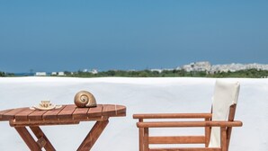 A wooden table with a shell and a plate, a wooden chair, and a white surface against a clear sky. - My Villa Naxos II (Naxos)