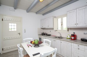 Une cuisine avec des armoires blanches, un plan de travail blanc, un évier et une cuisinière. On peut voir un saladier rempli de fruits sur le plan de travail et une télécommande sur la table.
