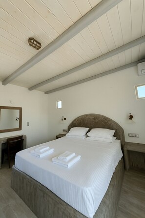 Une chambre à coucher avec un grand lit, une tête de lit en bois, une table de chevet, une commode, un miroir et un luminaire au plafond.