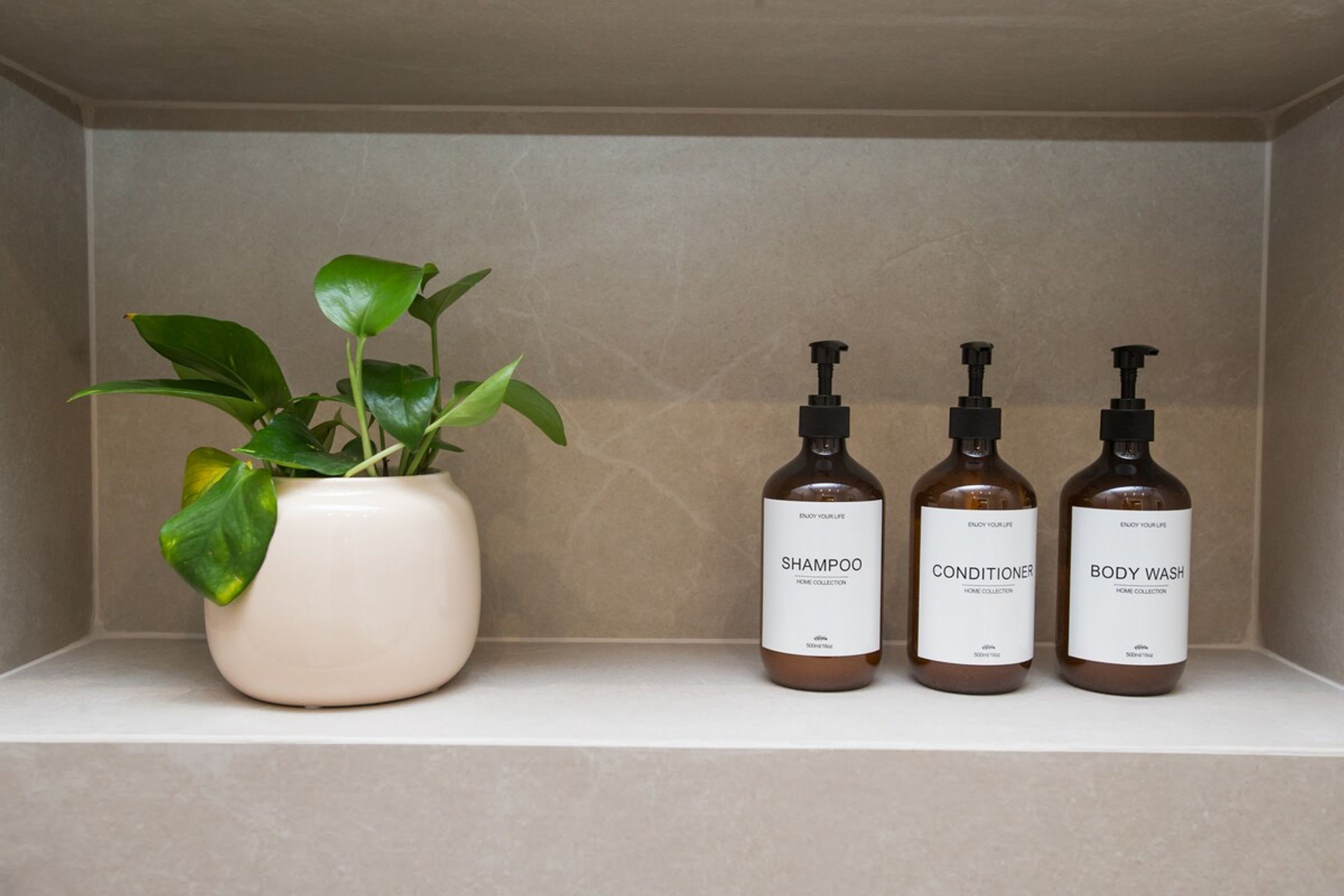 Une étagère avec un pot de plante et trois bouteilles de produits de toilette.