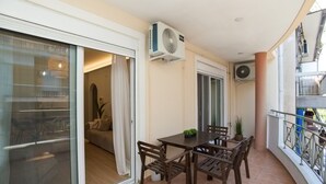 A balcony with a dining table and chairs, a sliding glass door leading to a living area, and an air conditioning unit. - K11 Apartment (Athens)
