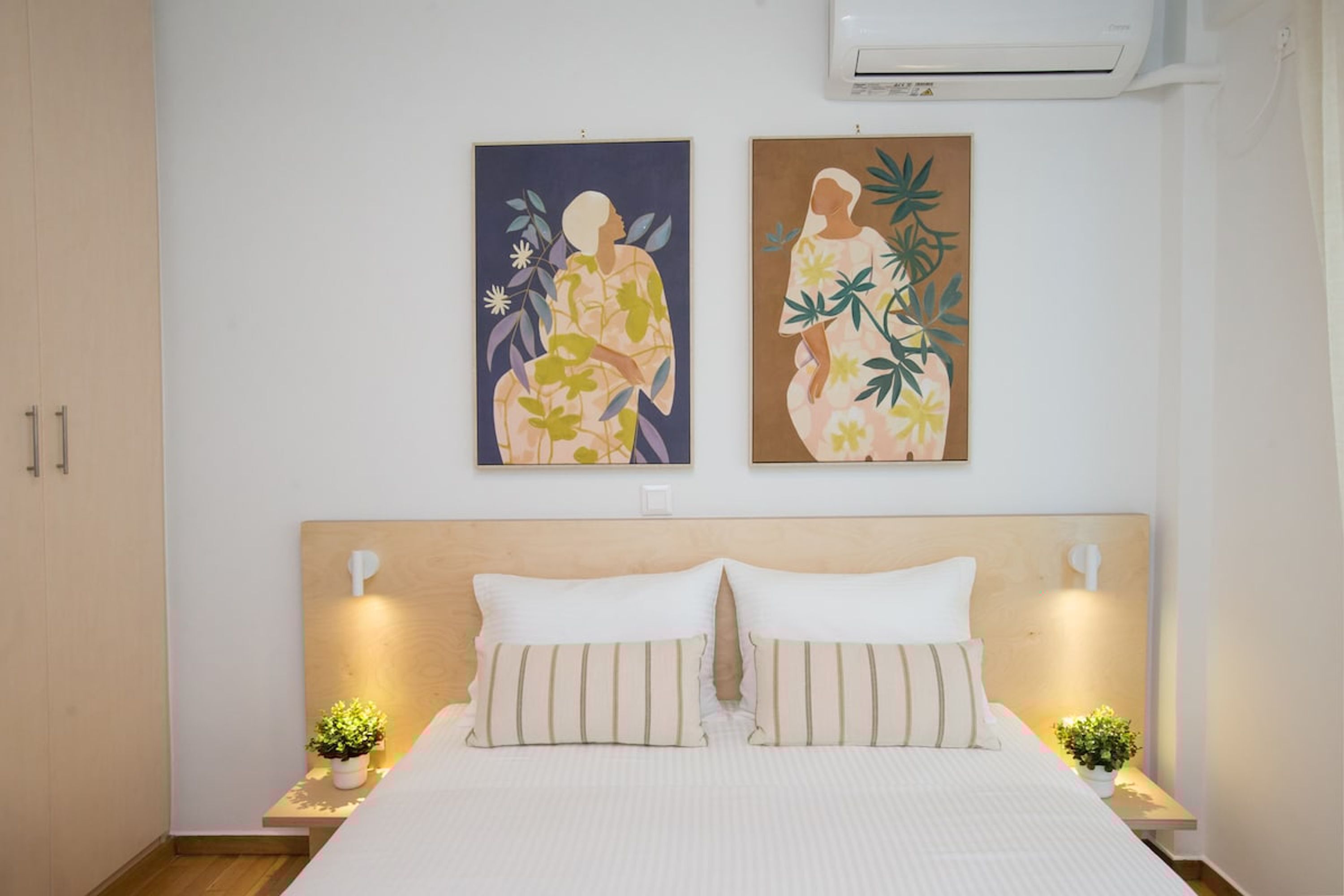A bedroom with a bed, two nightstands, two wall-mounted lamps, and two wall art pieces.