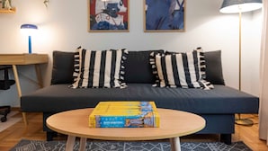 Un salon moderne avec un canapé bleu foncé, des coussins à rayures, une table basse en bois et deux tableaux abstraits accrochés au mur.