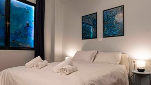 Un lit bien fait, avec deux serviettes enroulées, une lampe de chevet et deux tableaux abstraits accrochés au mur.