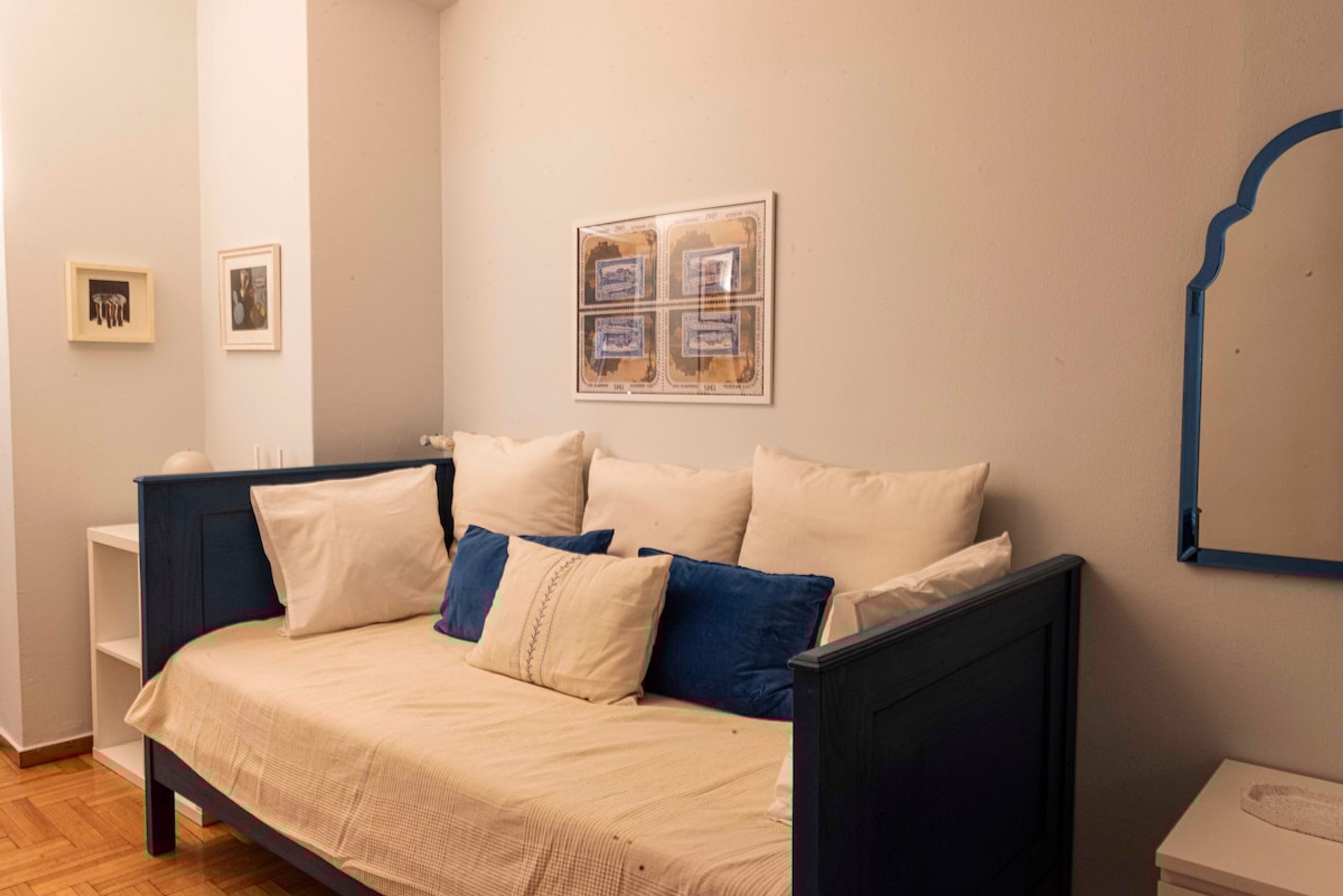 Un dormitorio con cama, almohadas, una mesita de noche, un espejo adosado a la pared y obras de arte enmarcadas.