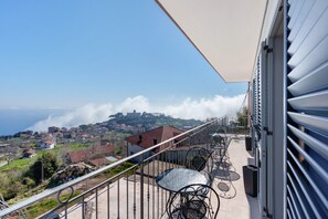 Un balcón con vistas a un pueblo costero, mobiliario exterior y barandilla.