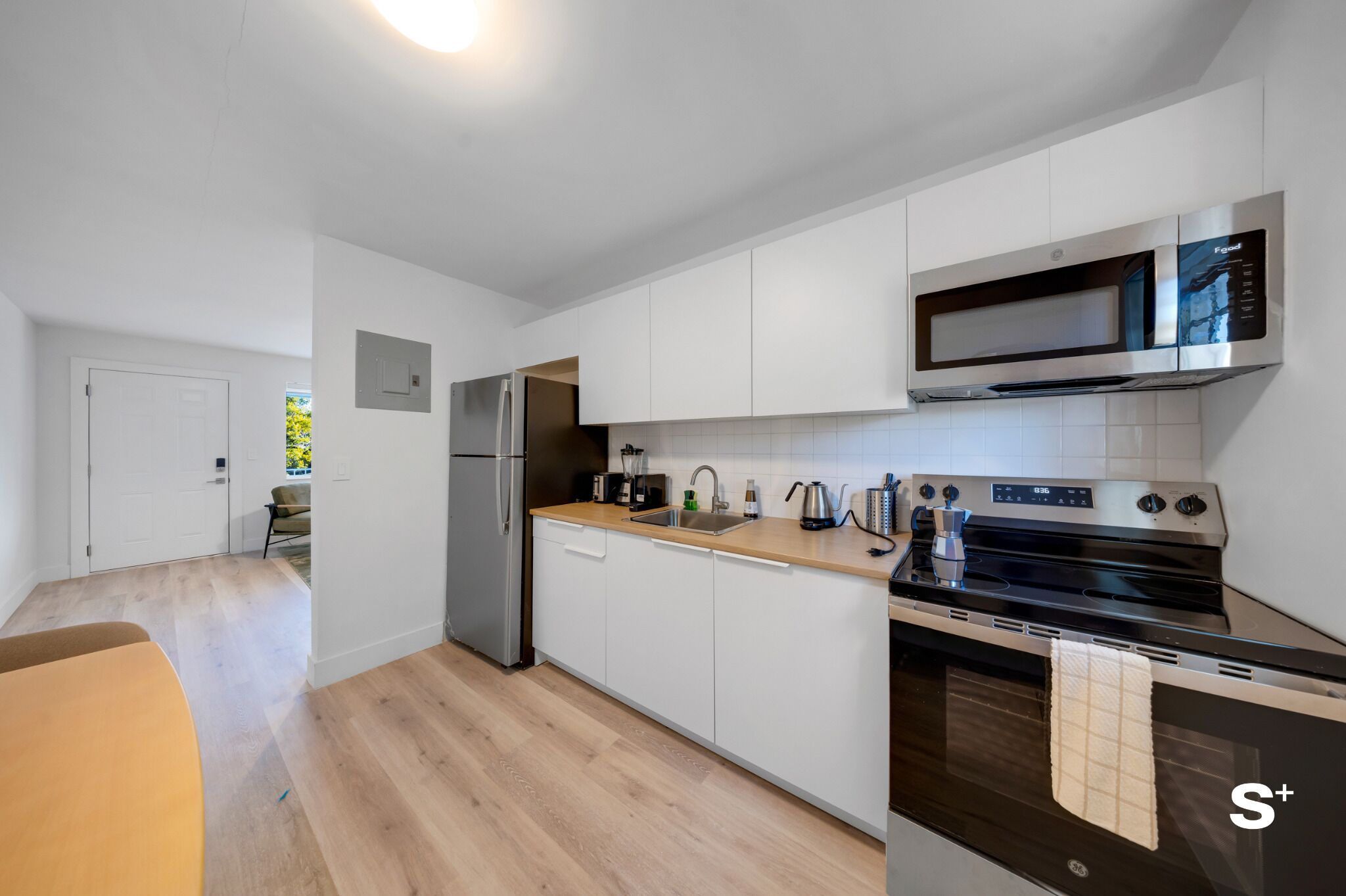 Una cocina moderna con armarios blancos, un refrigerador de acero inoxidable, un microondas y un horno.