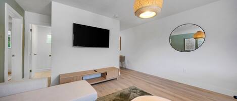 Un salón moderno con televisor de pantalla plana, un espejo redondo y una lámpara de techo trenzada.
