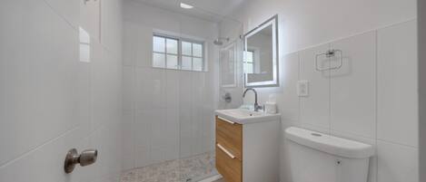 Un baño moderno con ducha de vidrio, tocador de madera, inodoro blanco y espejo sobre el lavabo.
