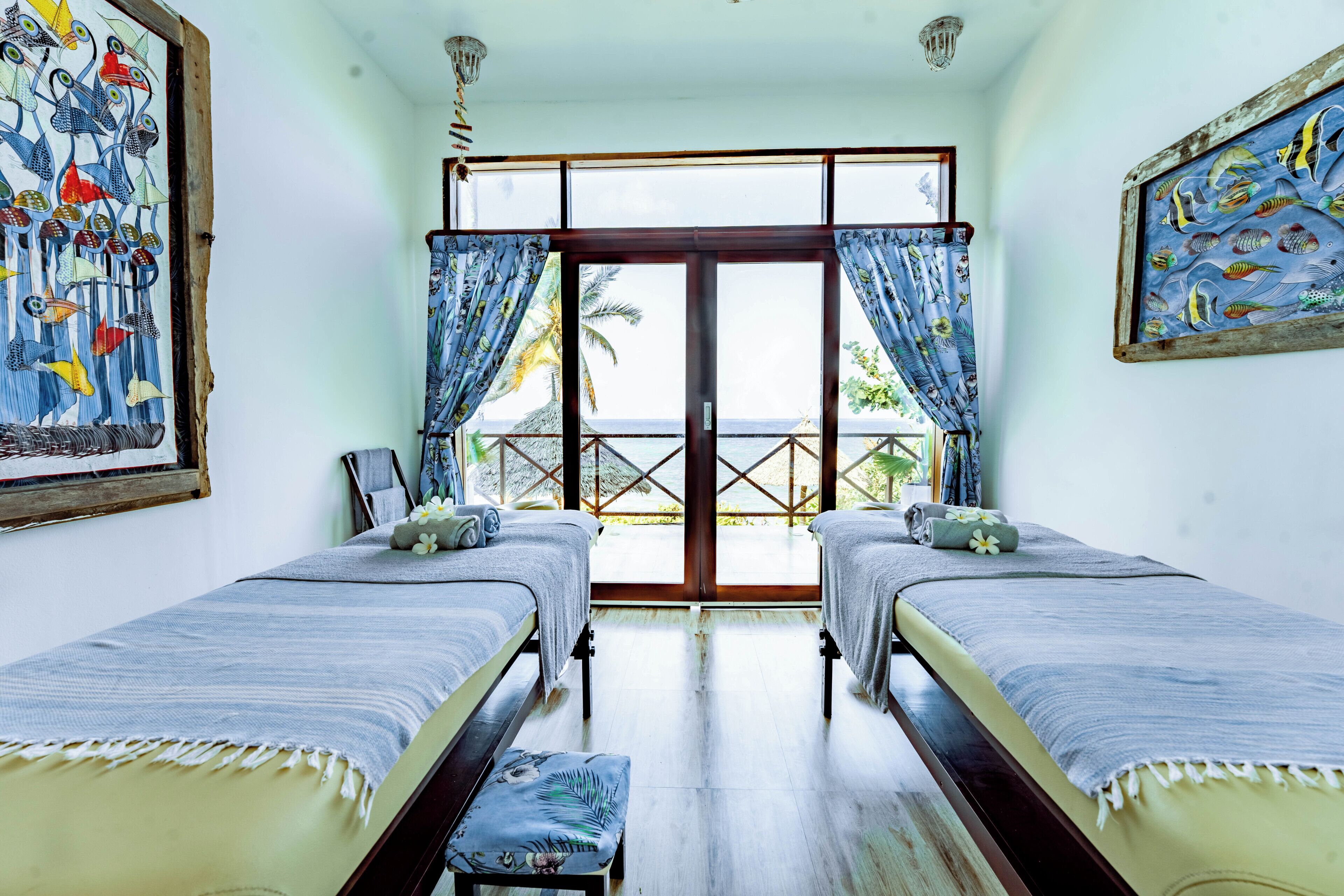 A room with two beds, a large window with curtains, and artwork on the walls.