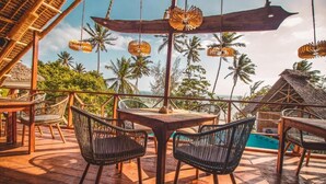 Une terrasse en bois avec une table et des chaises, donnant sur une piscine et des palmiers.