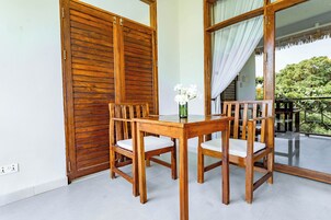 Una mesa de comedor de madera con sillas, un florero con flores y vista a la vegetación a través de un ventanal.