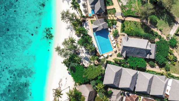 Vue aérienne d’un complexe hôtelier doté d’une piscine, d’une plage et d’une végétation tropicale.