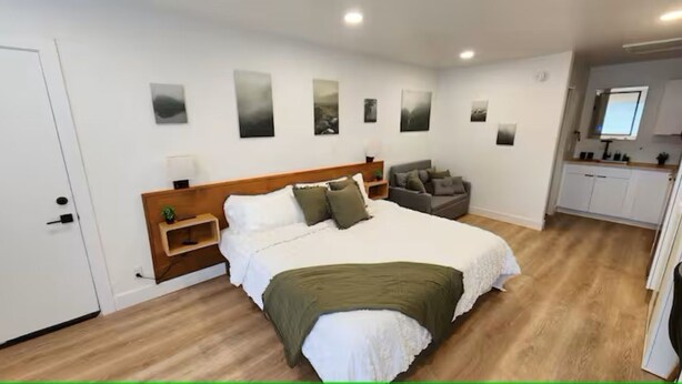 Een slaapkamer met een bed, nachtkastje, stoel en een kitchenette.