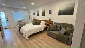 Een slaapkamer met een bed, een grijze bank, een nachtkastje en een raam met zonwering.