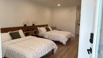 Une chambre d’hôtel avec deux lits, un plancher en bois, des murs blancs et des luminaires au plafond.