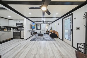 A modern kitchen with a central island, a dining area with a sofa and coffee table, and a large window providing a view.