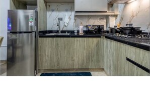 A modern kitchen with light wood cabinets, a stainless steel refrigerator, a marble backsplash, and a black countertop. - Charming apartment in beautiful Nairobi Kilimani with easy city access (Nairobi)