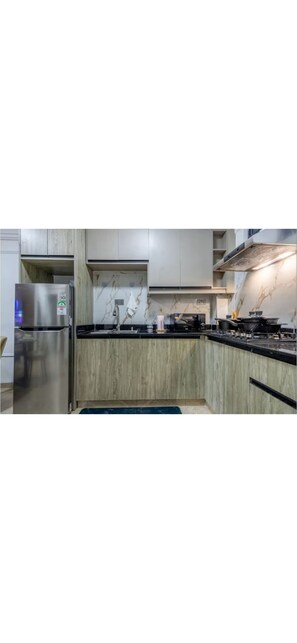 Eine moderne Küche mit hellen Holzschränken, einem Edelstahlkühlschrank, einer Marmor-Spritzschutzleiste und einer schwarzen Arbeitsplatte.