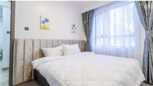 A neatly made bed with a white duvet, a headboard with a tufted design, and two wall-mounted floral paintings. - Charming apartment in beautiful Nairobi Kilimani with easy city access (Nairobi)