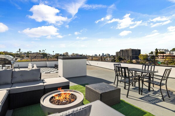 A rooftop terrace with outdoor furniture, a fire pit, and a view of the city skyline.