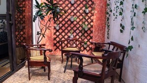 Un rincón acogedor con sillas de madera y una mesa, rodeado de plantas en macetas y una pared con celosía.