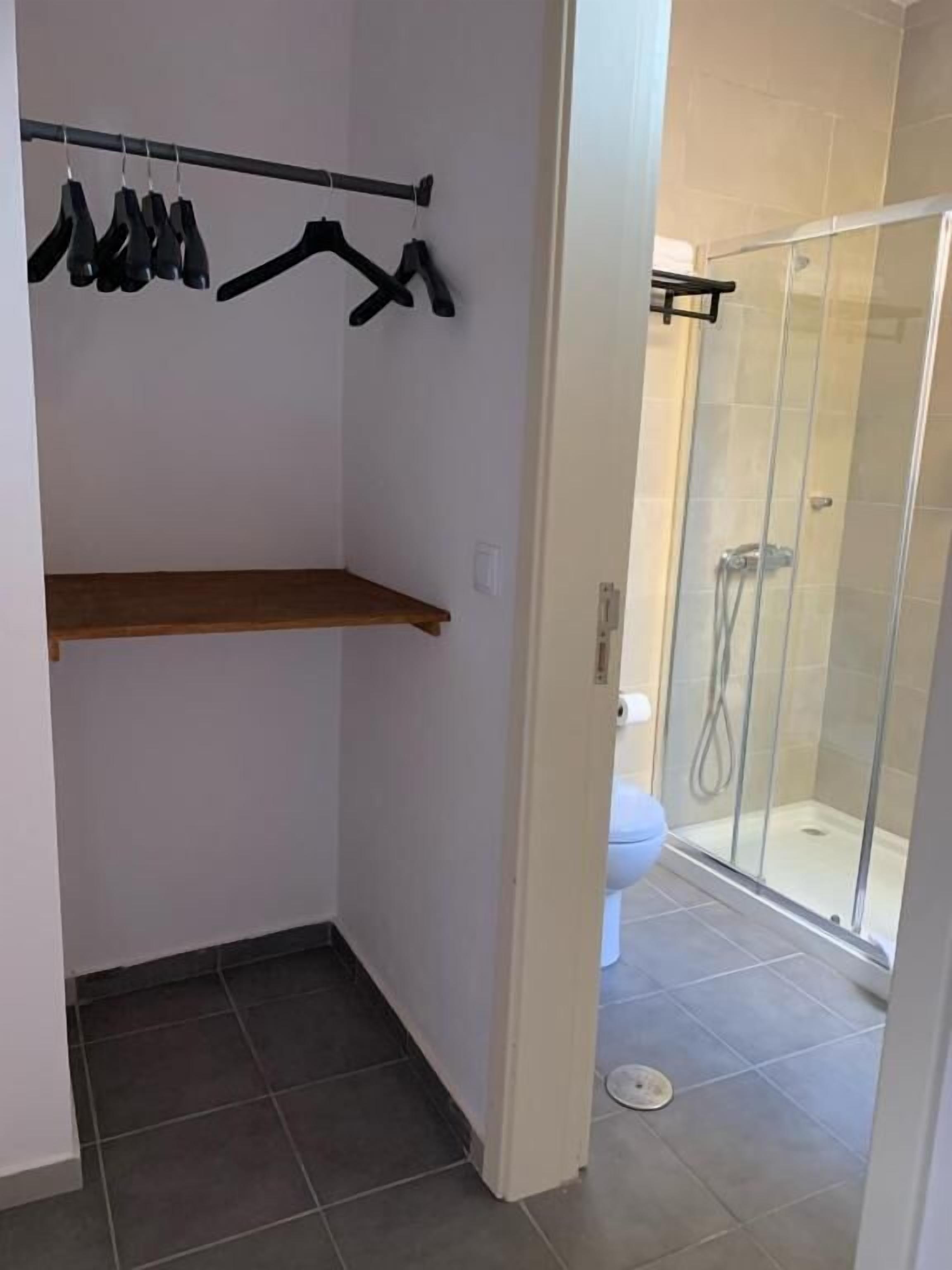 A small bathroom with a shower, a toilet, and a clothing rack with hangers.