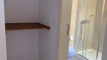 A small bathroom with a shower, a toilet, and a clothing rack with hangers.